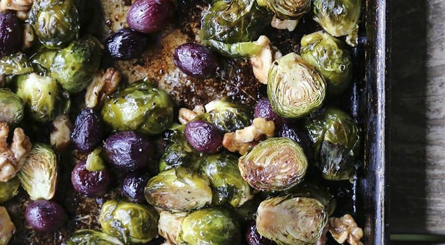 Roasted Brussels Sprouts with Walnuts and Grapes on antique metal sheet pan, wooden table, maldon sea salt