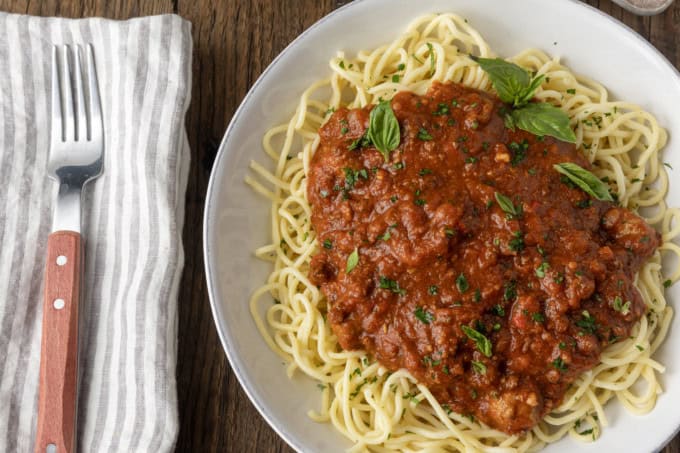 spaghetti sauce on spagetti on a plate topped by fresh herbs with a napkin and fork on the left.