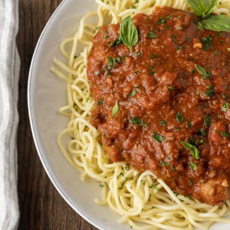 spaghetti sauce on spagetti on a plate topped by fresh herbs with a napkin and fork on the left.