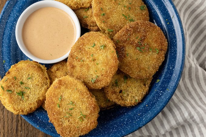 fried green tomatoes stacked on a blue enamel plate with a bowl of dip