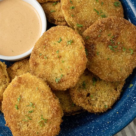 fried green tomatoes stacked on a blue enamel plate with a bowl of dip