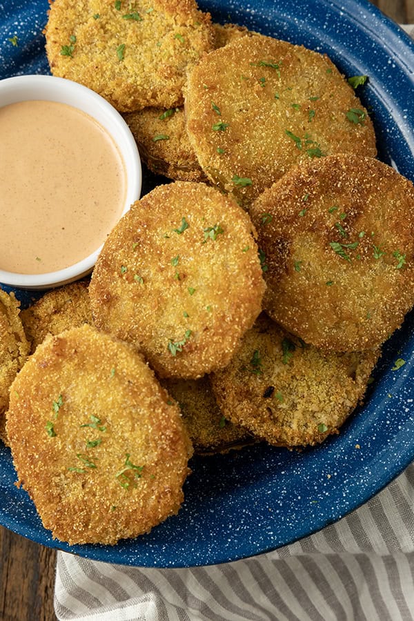 fried green tomatoes stacked on a blue enamel plate with a bowl of dip