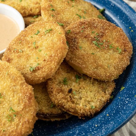 fried green tomatoes stacked on a blue enamel plate with a bowl of dip