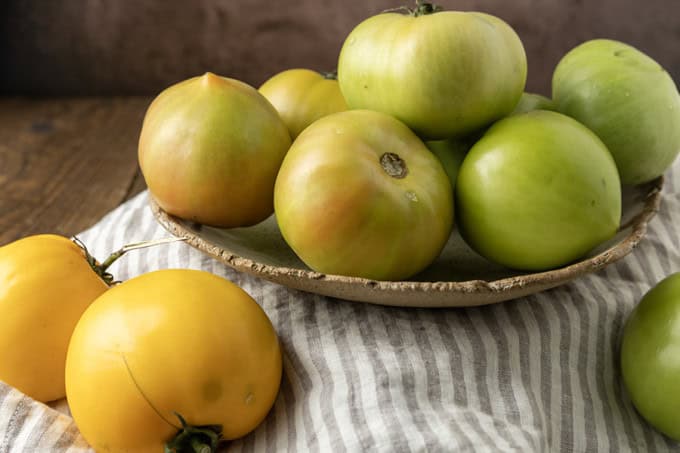 green tomatoes in a pottery bowl with a taupe and white striped linen