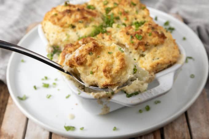 small white casserole dish filled with sausage gravy and topped with buttermilk biscuit crust on top of a plate with a spoon in it.